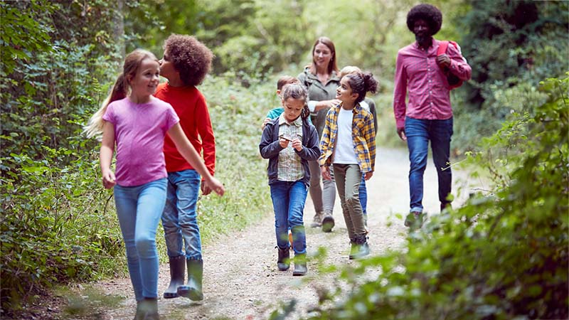 Adult Walking With Group Of Children On Dirt Path