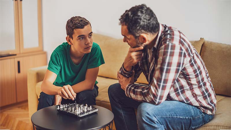 Child and man play chess while talking